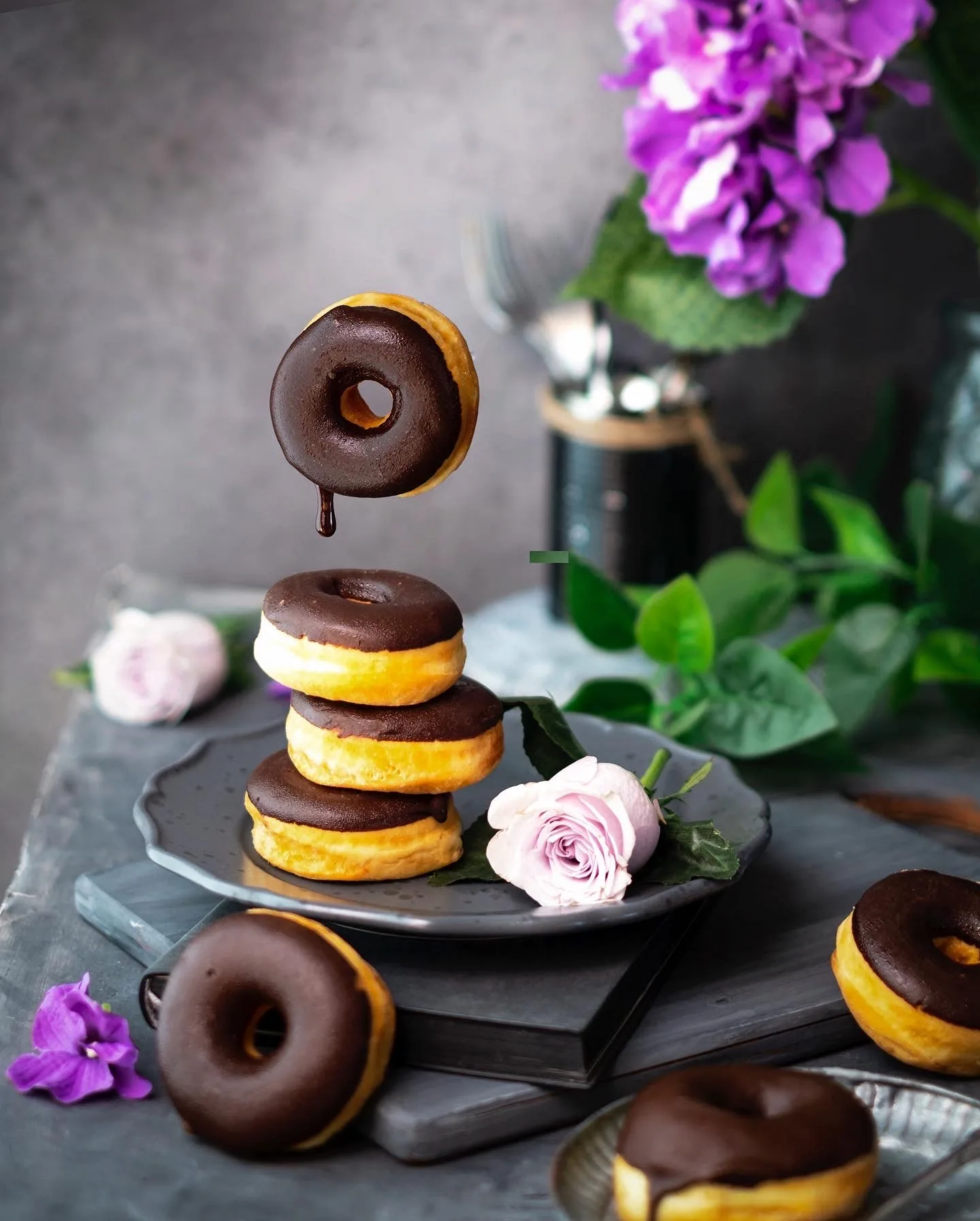 Stack of chocolate-glazed donuts with flowers on a dark background – dessert photography, Dubai