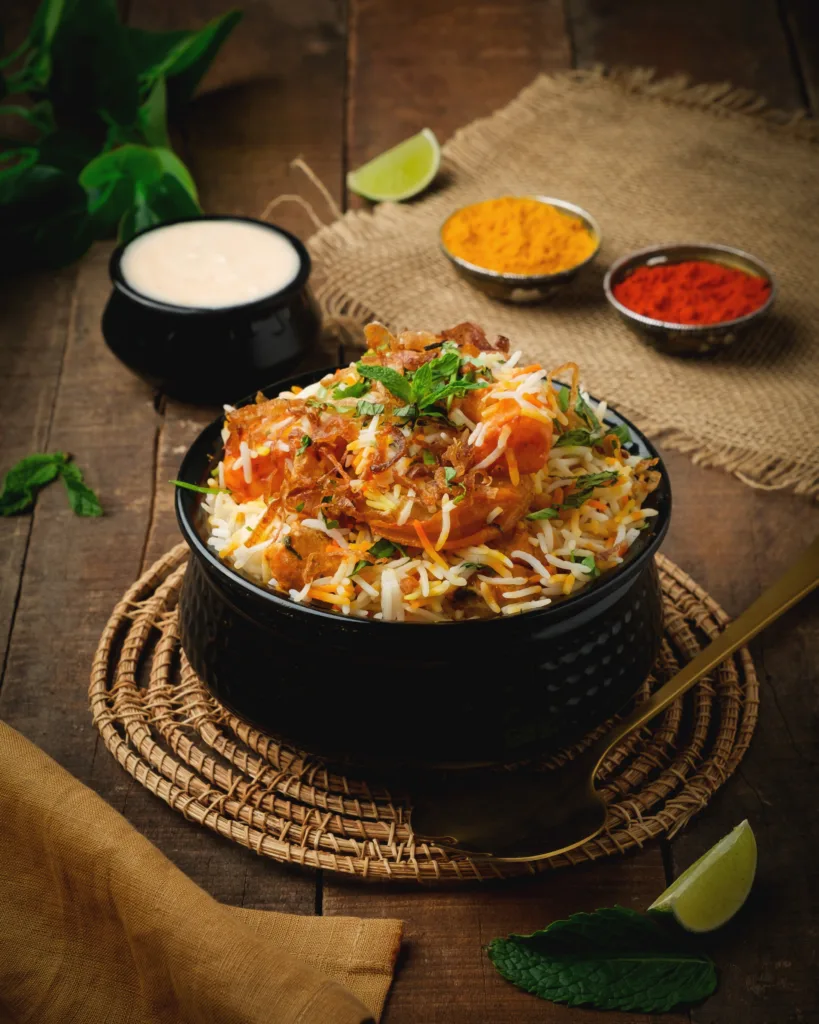 Chicken biryani in a black bowl with raita and condiments – Indian restaurant menu photography, Dubai