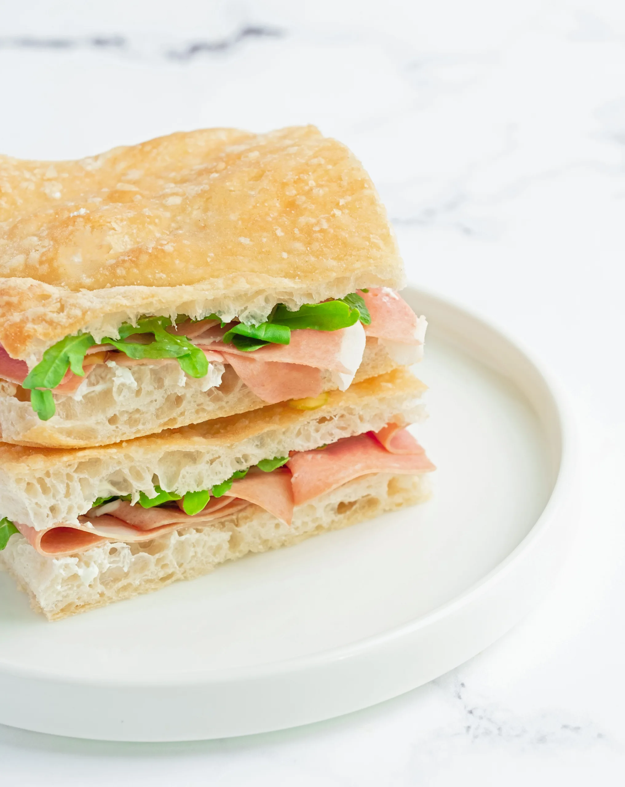 Layered ciabatta sandwich with prosciutto and cream cheese on a white plate – café menu photography, Dubai
