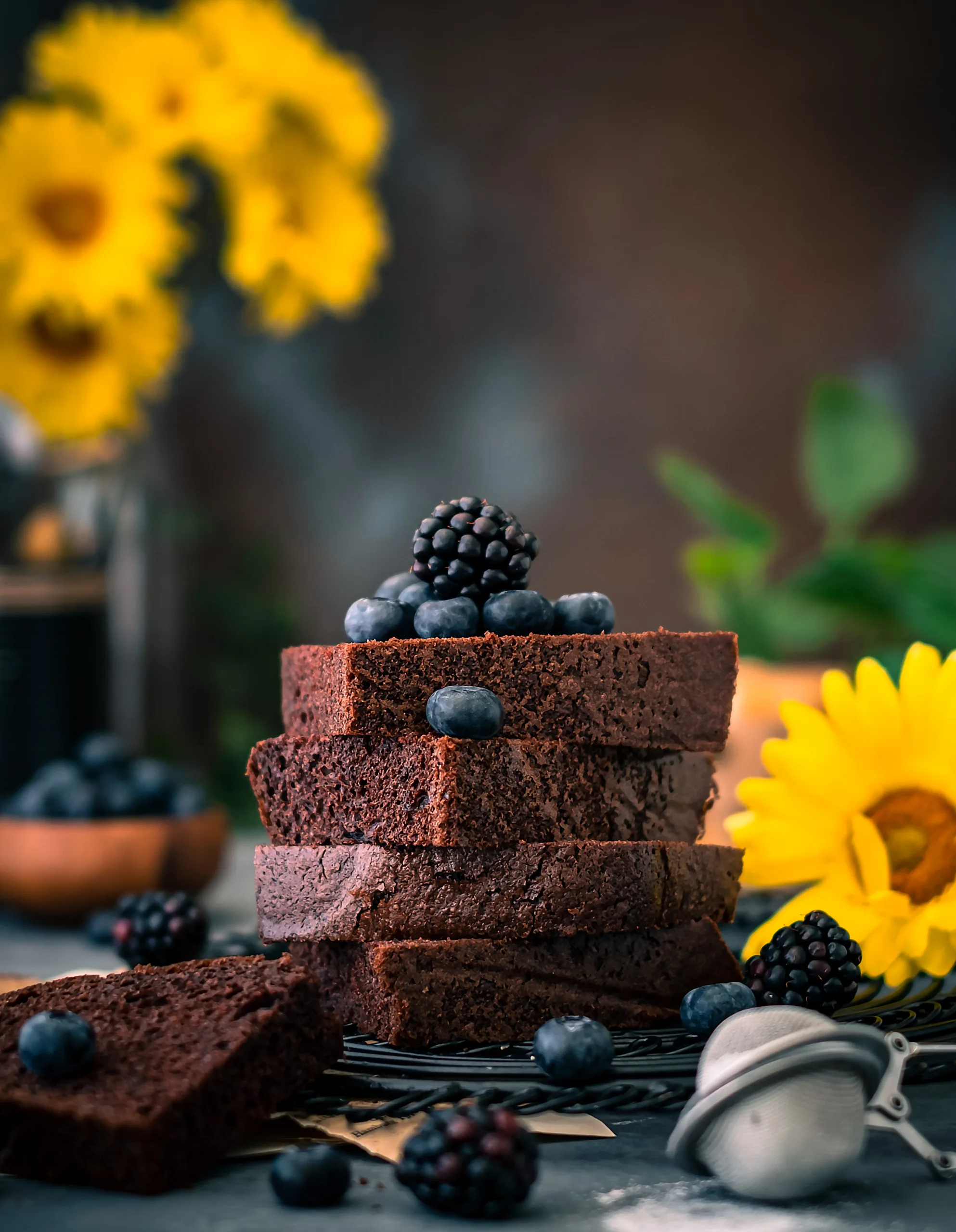 Stacked chocolate brownie slices topped with blueberries and blackberries – dark and moody dessert photography, Dubai