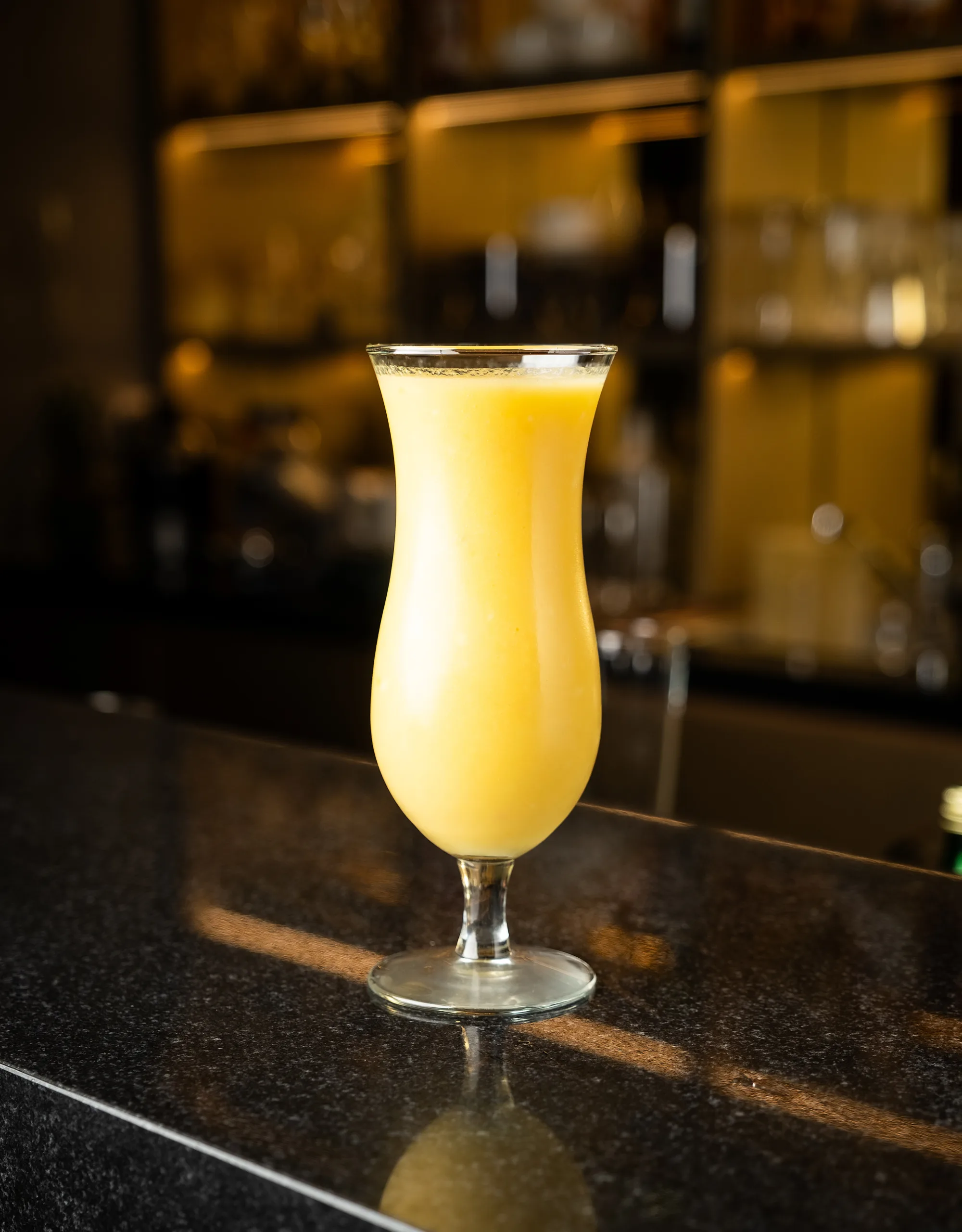 Yellow mango smoothie in a hurricane glass at a bar – beverage photography, Dubai