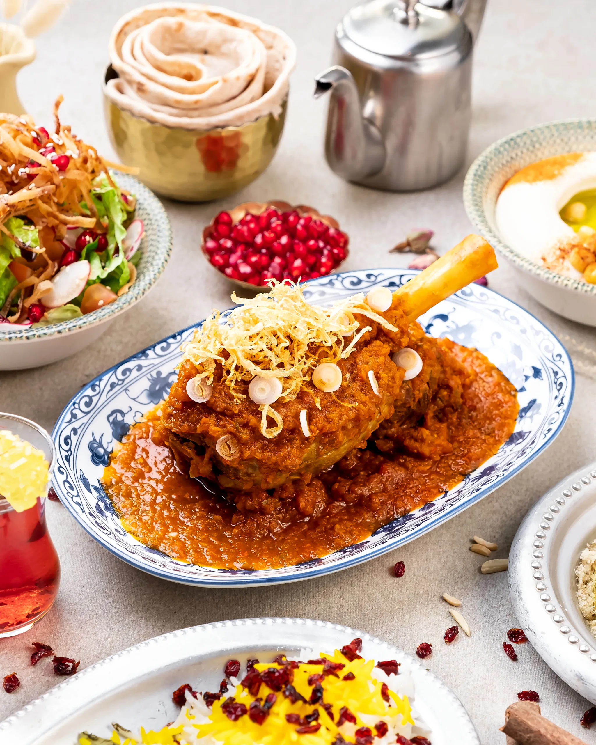 Braised lamb shank on a blue-and-white plate with pomegranate and crispy onions – restaurant menu photography, Dubai