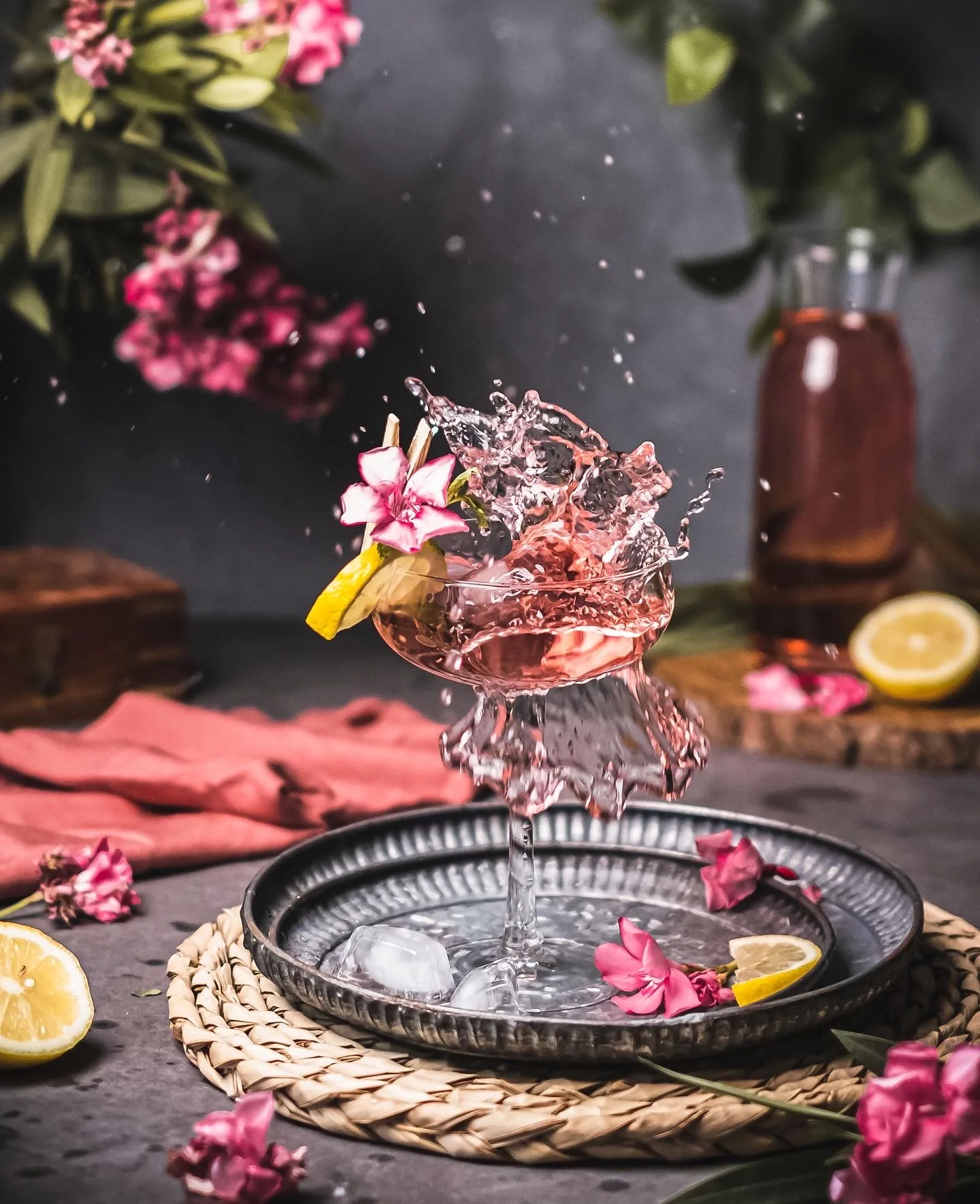 Pink drink splashing out of a glass on a silver tray with flowers – splash photography, Dubai