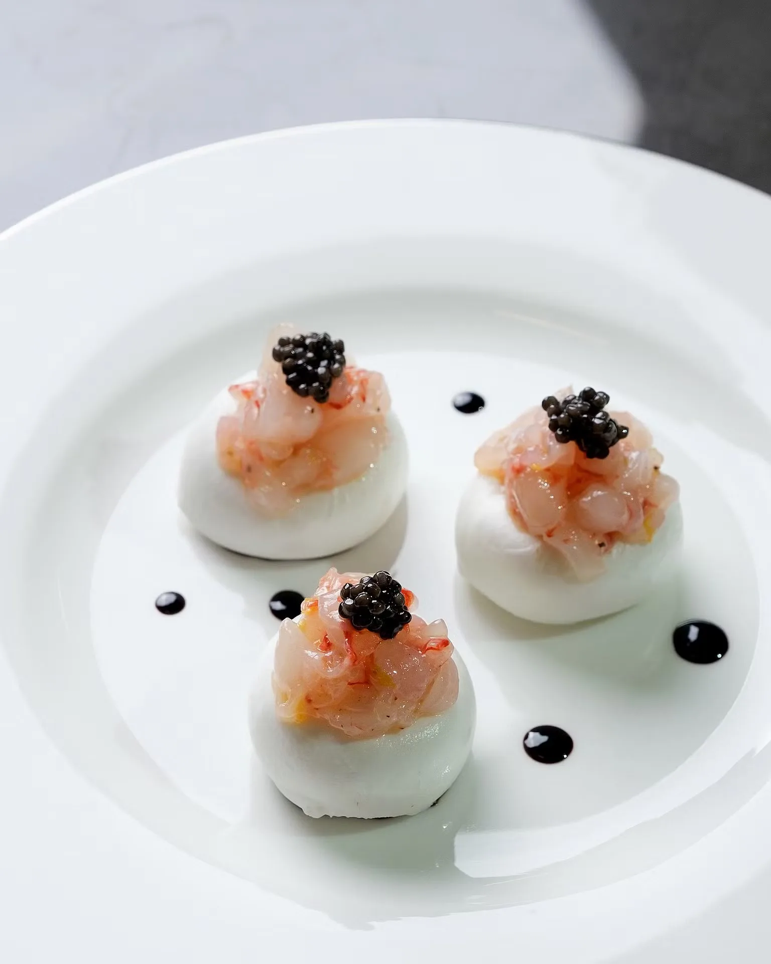 Prawn tartare bites topped with black caviar on white plates – fine-dining food photography, Dubai