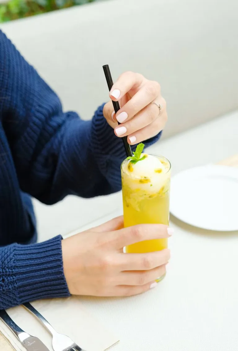 Hand stirring a yellow fizzy lemonade in a tall glass – beverage photography, Dubai