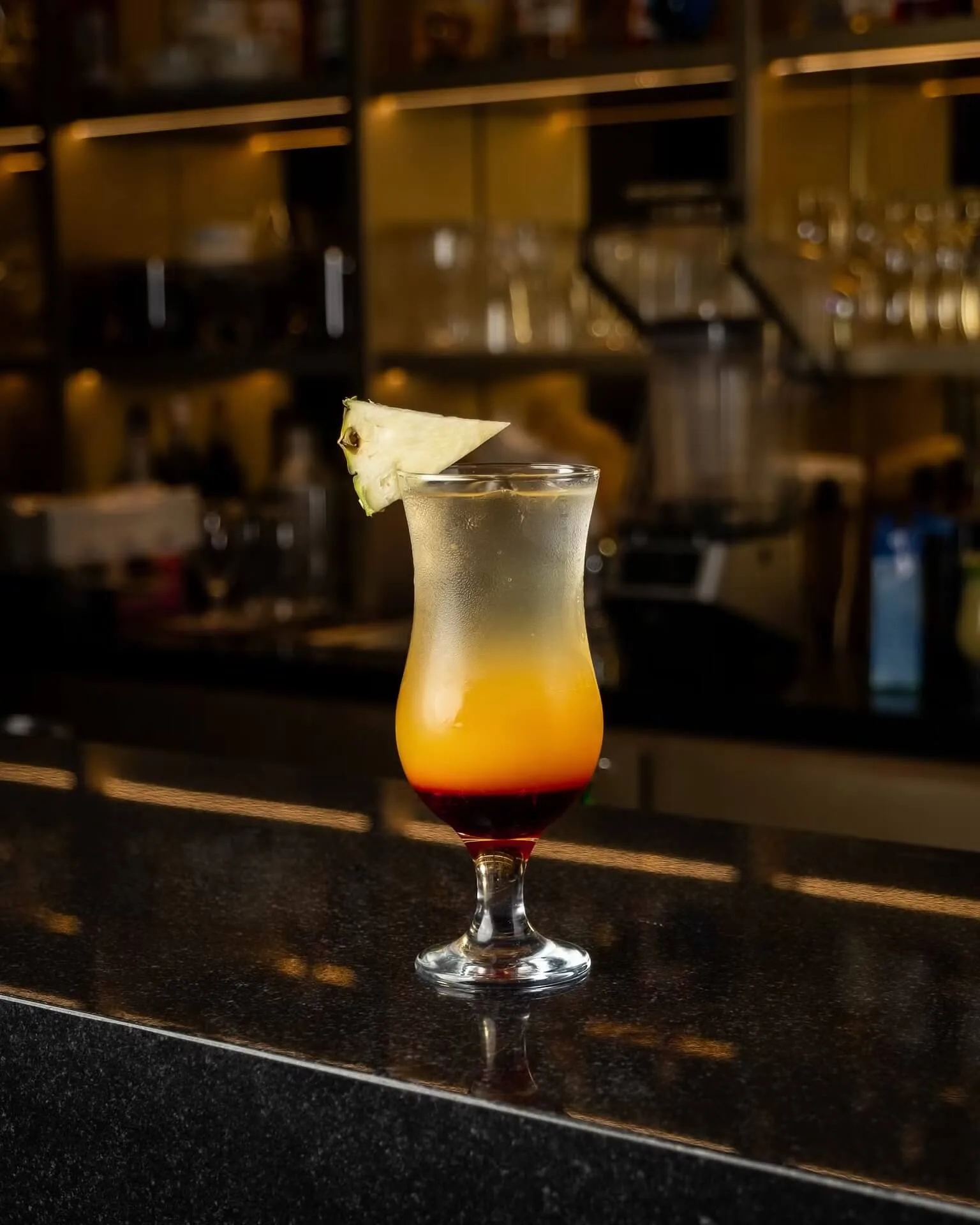 Orange and yellow layered cocktail with pineapple garnish at a bar – drink photography, Dubai