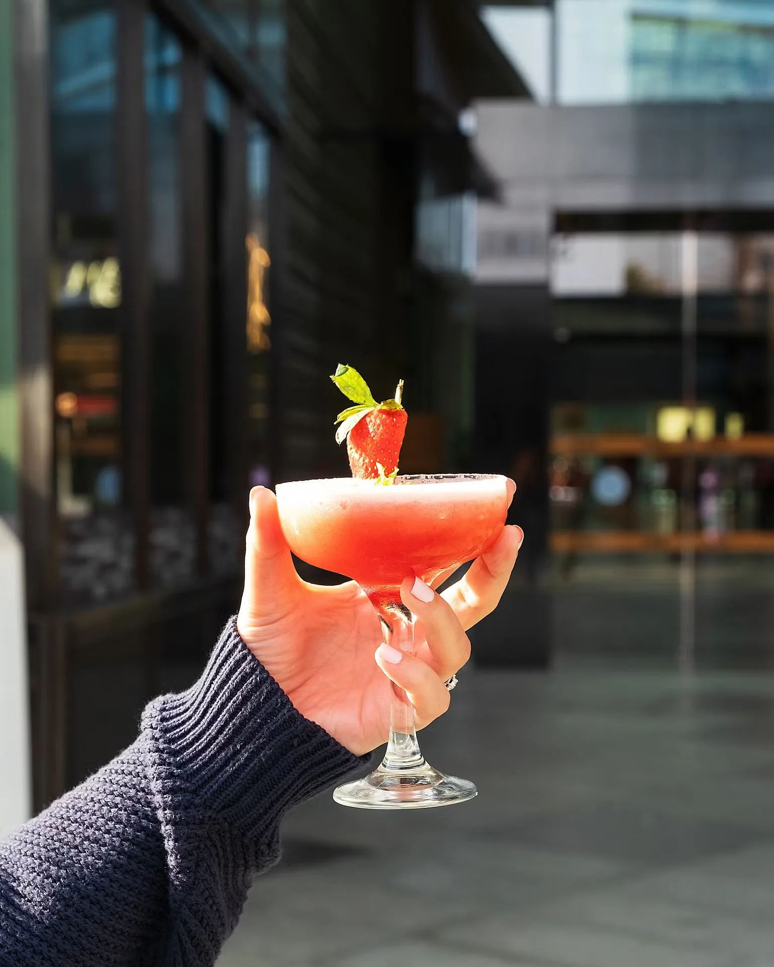 Hand holding a pink strawberry cocktail with a strawberry garnish – bar drinks photography, Dubai
